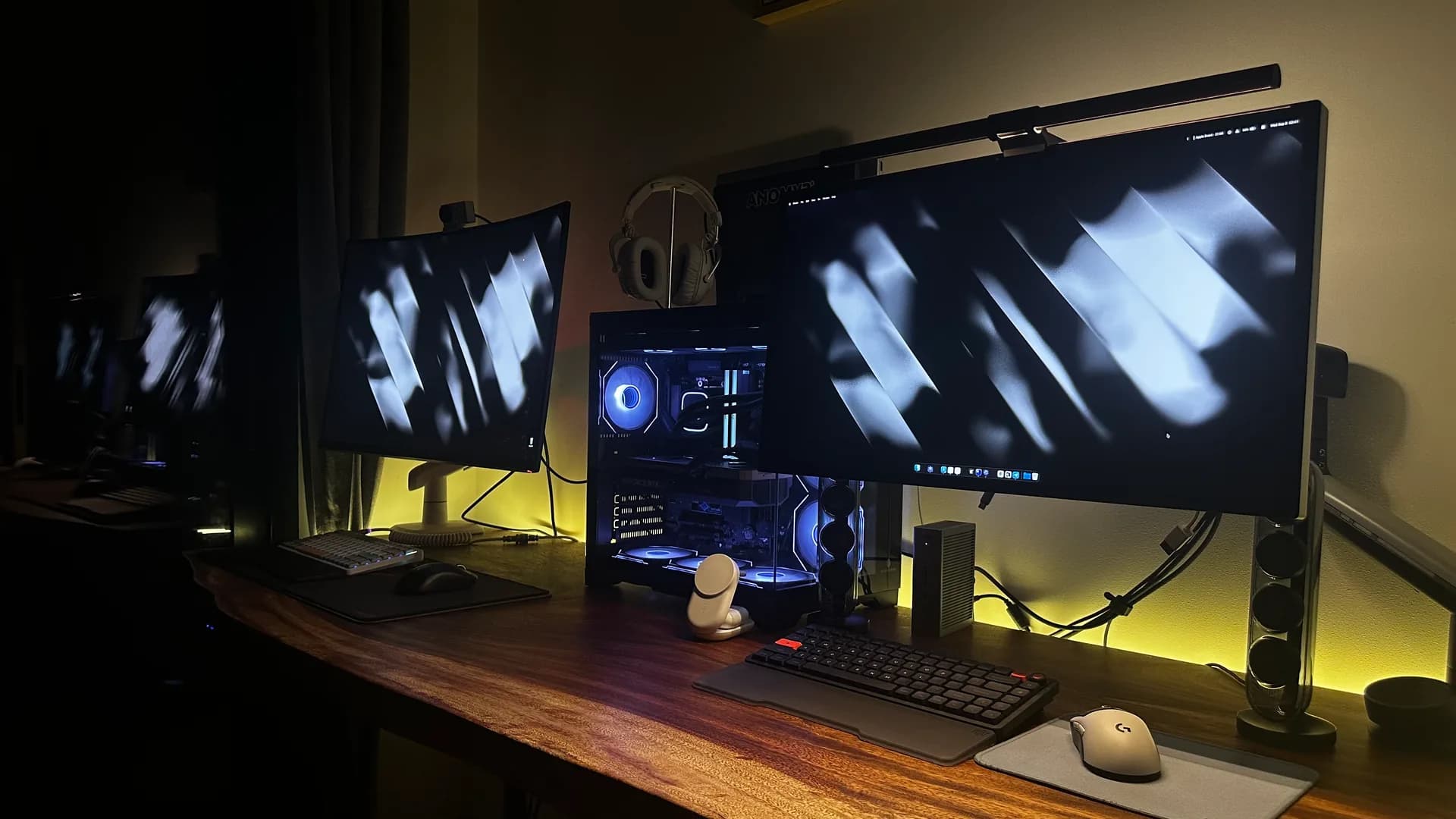 Desk setup with two monitors, keyboards, speakers and an illuminated desktop PC